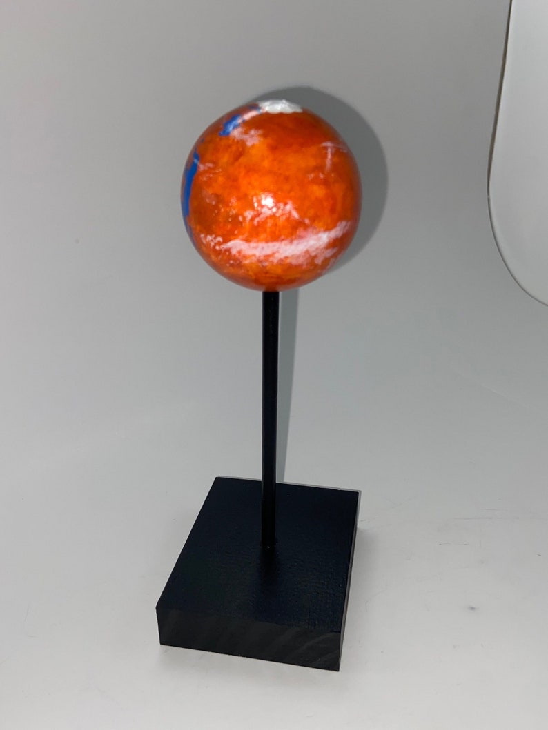Puede incluir: Un peque&ntilde;o globo naranja y blanco sobre un soporte negro. El globo est&aacute; pintado para parecerse a Marte.