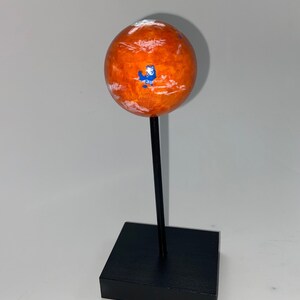 Puede incluir: Un peque&ntilde;o modelo de globo de Marte naranja y blanco en un soporte negro. El globo tiene marcas blancas y azules.