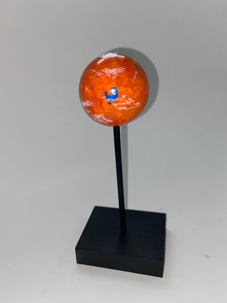 Puede incluir: Un peque&ntilde;o modelo de globo de Marte naranja y blanco en un soporte negro. El globo tiene marcas blancas y azules.