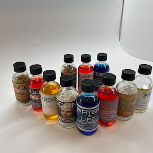 May include: A collection of small glass bottles with various colored liquids and solids inside. The bottles have labels with different text, including "Water of Life", "Evidence", "Juice of the Apocalypse", and "RDNA".