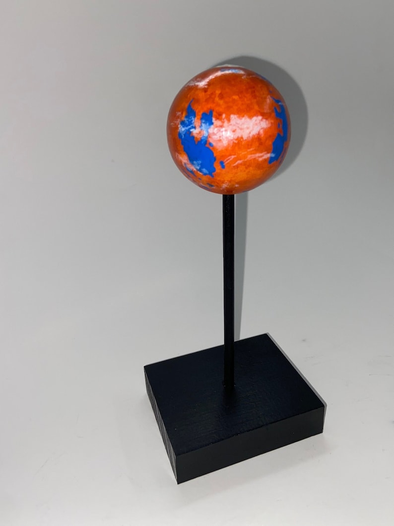 Puede incluir: Un peque&ntilde;o globo terr&aacute;queo naranja y azul sobre un soporte negro. El globo est&aacute; pintado para parecerse a Marte con nubes blancas y oc&eacute;anos azules.