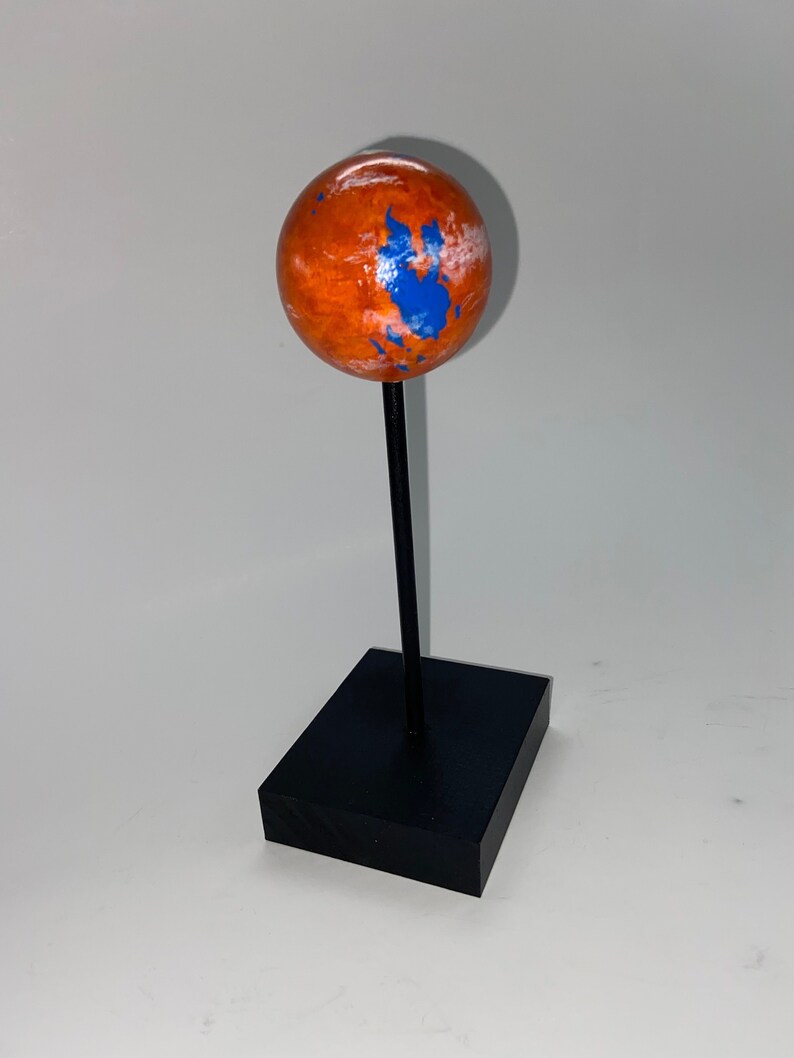 Puede incluir: Un peque&ntilde;o globo terr&aacute;queo naranja y azul sobre un soporte negro. El globo est&aacute; pintado para parecerse a Marte con nubes blancas y agua azul.