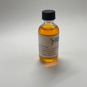 Puede incluir: Una pequeña botella de vidrio transparente con una tapa negra llena de un líquido dorado. La etiqueta de la botella dice "Sticke de Amrita", "R of Collection: 12/16/20", "Aloha Centaun", "Moon: Pandora", y "Reefs' Awa-attu".