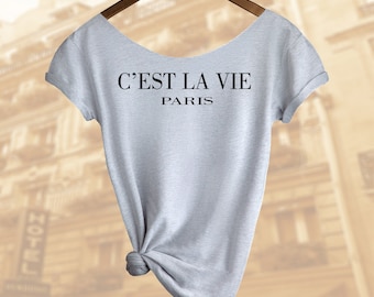 C'est la vie シャツ。フランス語の格言。パリシャツ。レディースオフショルダー スローピートップ。ユニセックスもあります。2 枚ご購入で 3 枚目のシャツが無料になります!!