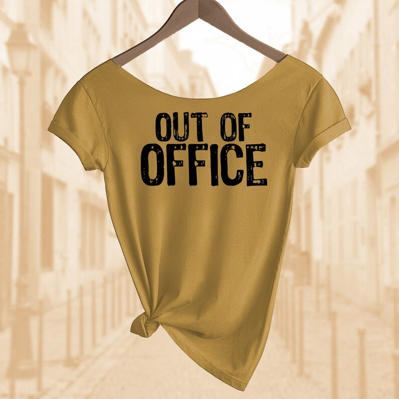 以下が含まれることがあります： マスタードイエローのTシャツに、黒い文字で「OUT OF OFFICE」とプリントされています。