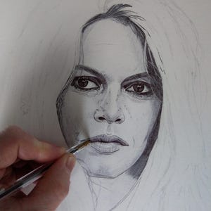 以下が含まれることがあります： 長い明るい髪の人物の鉛筆画の肖像画。 唇の近くにペンを持っている手があり、描画は進行中です。肖像画は、被写体の顔の特徴を捉え、詳細なシェーディングとハイライトを備えています。