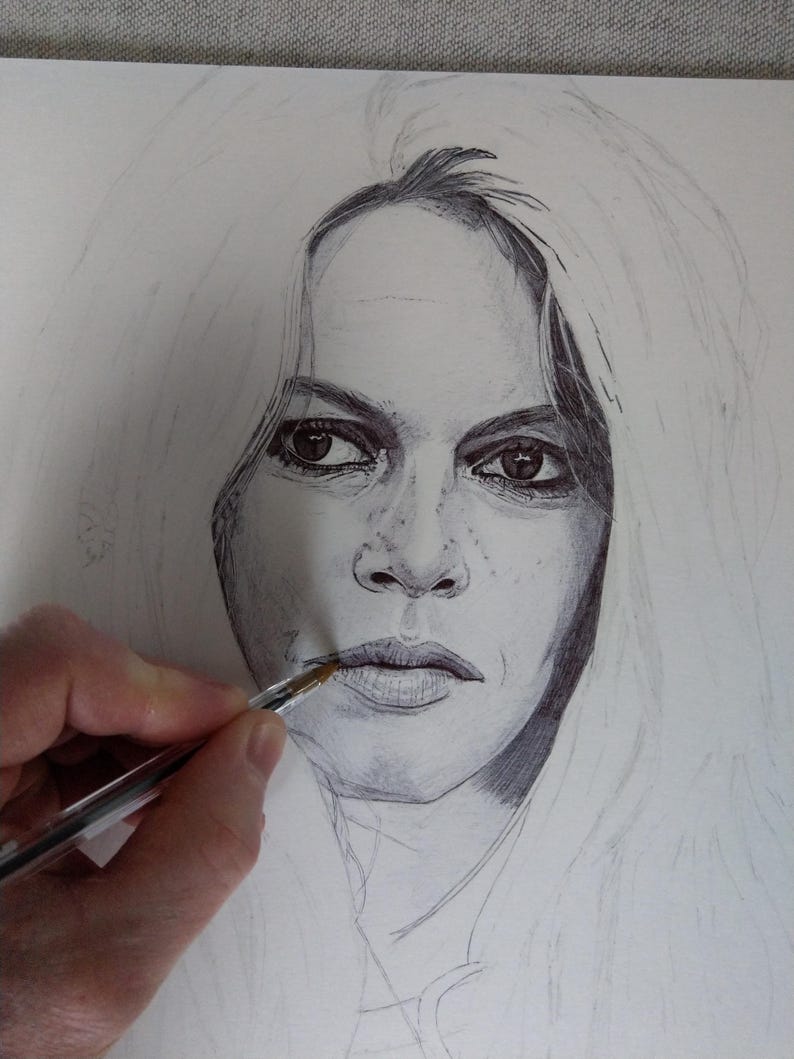 以下が含まれることがあります： 長い明るい髪の人物の鉛筆画の肖像画。 唇の近くにペンを持っている手があり、描画は進行中です。肖像画は、被写体の顔の特徴を捉え、詳細なシェーディングとハイライトを備えています。