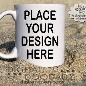 May include: White ceramic mug with a black outline of the text "PLACE YOUR DESIGN HERE". The mug is sitting on a sandy beach.