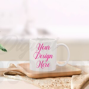 May include: White ceramic mug with a pink inscription that reads "Your Design Here" on a wooden coaster and a white cloth napkin.