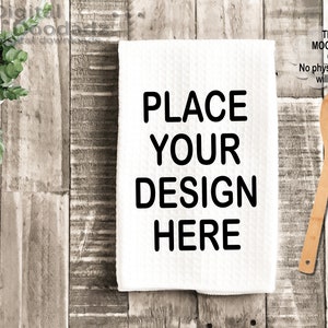 May include: White kitchen towel with the text "PLACE YOUR DESIGN HERE" in black, a wooden spoon, and a small potted plant on a rustic wooden surface. The image includes the text "This is a MOCK UP file ONLY No physical product will be sent."