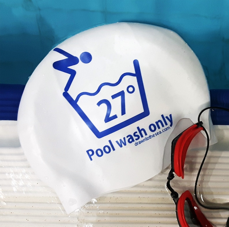 May include: White swim cap with blue text that reads "Pool wash only 27&deg; drawn to the sea.com". A red and black swimming goggle is partially visible in the bottom right corner of the image.