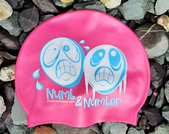May include: Pink swim cap with a blue and white graphic of two cartoon faces with the text "Numb & Number drawn to the sea.com".
