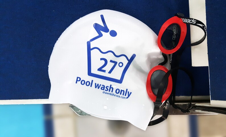 May include: White swim cap with a blue washing instruction icon that says "Pool wash only" and "27&deg;" with a website address. Red swimming goggles with a black strap.