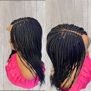May include: Two images of a black braided wig. The wig features small, tightly woven braids, with a lace front. The wig is styled with the braids falling down the back. The wig is displayed on a mannequin head, with a pink top.