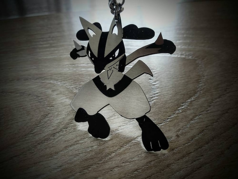 May include: A silver-colored pendant in the shape of a cartoon character with black accents. The pendant is suspended from a silver chain. The character has pointed ears, a black mask, and is in a fighting pose.