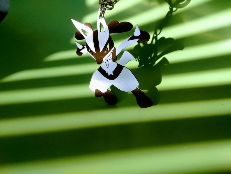 May include: A brown and white Lucario keychain, suspended from a silver chain. The character is in a dynamic pose, with sharp angles and a star-shaped emblem on its chest. The background is a vibrant green with striped shadows.