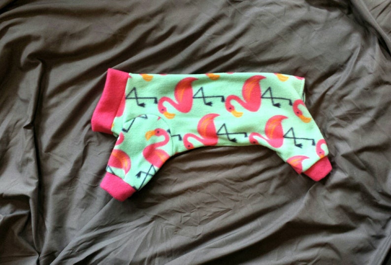 May include: Green fleece dog pajamas with a pink flamingo print.