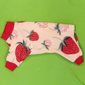 May include: A pink and red dog pajamas with a strawberry print. The pajamas have red trim around the neck and sleeves.