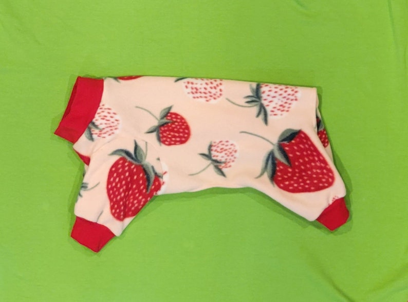 May include: A pink and red dog pajamas with a strawberry print. The pajamas have red trim around the neck and sleeves.