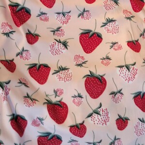 May include: A pink fabric with a repeating pattern of red and white strawberries. The strawberries are stylized and have a white outline.