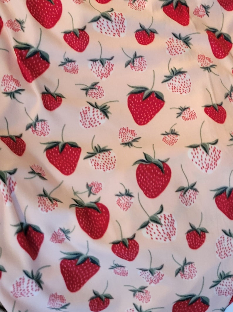 May include: A pink fabric with a repeating pattern of red and white strawberries. The strawberries are stylized and have a white outline.