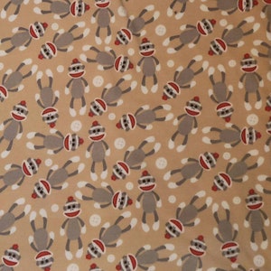 May include: A tan fabric with a repeating pattern of gray sock monkeys wearing red hats. The monkeys are in various poses with their arms and legs outstretched.
