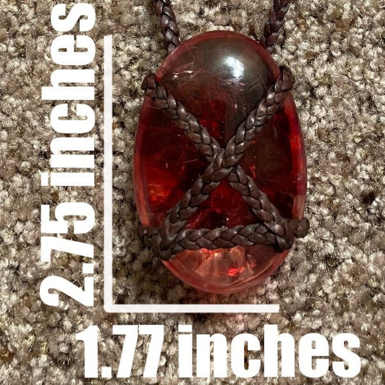 May include: A red glass pendant with a brown leather cord, measuring 2.75 inches by 1.77 inches.