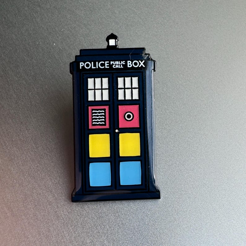 Pode incluir: Um &iacute;man azul marinho da cabine da pol&iacute;cia com as palavras "POLICE PUBLIC CALL BOX" no topo. O &iacute;man tem janelas brancas, um quadrado vermelho com um c&iacute;rculo branco e quadrados amarelos e azuis.