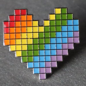 Può includere: Uno spillo a forma di cuore pixelato arcobaleno. Il cuore è composto da piccoli quadrati nei colori dell'arcobaleno, dal rosso al viola.