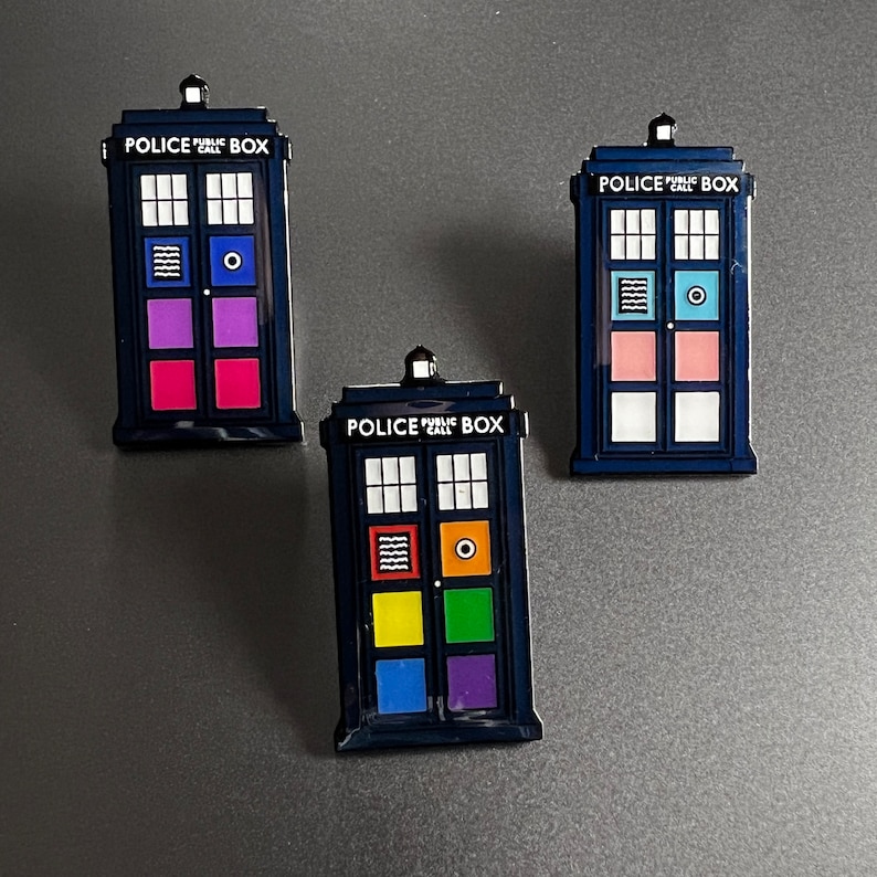 Pode incluir: Tr&ecirc;s &iacute;manes azuis marinhos em forma de cabine telef&oacute;nica da pol&iacute;cia, com pain&eacute;is coloridos. Cada &iacute;man apresenta o texto "POLICE CALL BOX" acima das janelas. Os pain&eacute;is s&atilde;o de v&aacute;rias cores, incluindo rosa, roxo, azul, amarelo e laranja.
