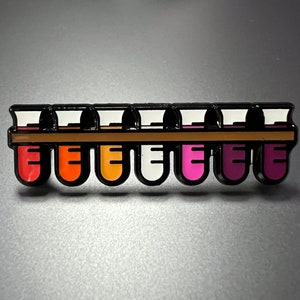 May include: A rainbow pride flag is represented by a row of seven test tubes, each filled with a different color of the flag: red, orange, yellow, white, pink, purple, and blue. The test tubes are held in a black rack with a brown bar.