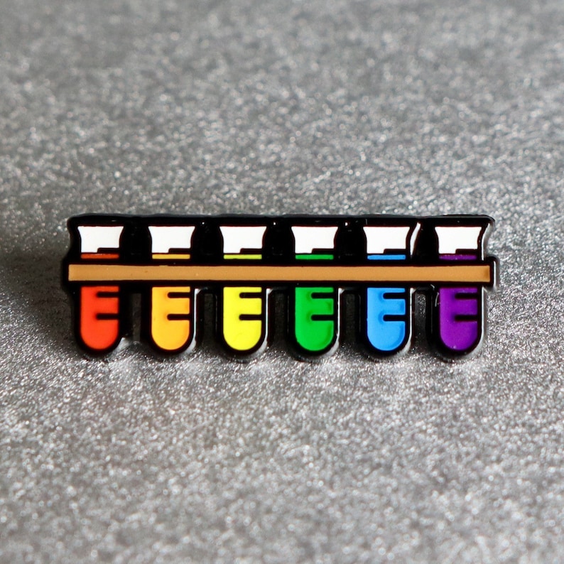 K&ouml;nnte beinhalten: Eine Regenbogen-Emaille-Anstecknadel mit einer Reihe von acht Reagenzgl&auml;sern, die jeweils mit einer anderen Farbe Fl&uuml;ssigkeit gef&uuml;llt sind. Die Reagenzgl&auml;ser sind in einem Regenbogenmuster angeordnet, mit Rot, Orange, Gelb, Gr&uuml;n, Blau, Indigo und Violett.