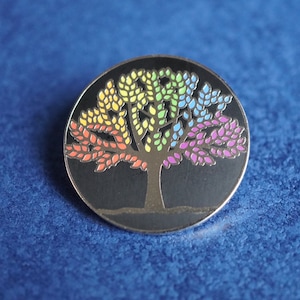 May include: A rainbow coloured tree pin with a black background. The tree is made of metal and has a shiny finish.
