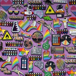 Pode incluir: Uma cole&ccedil;&atilde;o de alfinetes de esmalte coloridos com v&aacute;rios designs, incluindo arco-&iacute;ris, astronautas, c&eacute;rebros e textos como "SCIENTIST", "HE HIM", "THEY THEM" e "QUEER". Os alfinetes est&atilde;o dispostos sobre um fundo roxo.