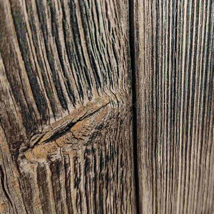 May include: Close-up of a weathered wooden surface with a knot in the center. The wood has a natural brown and gray color with a rough texture.
