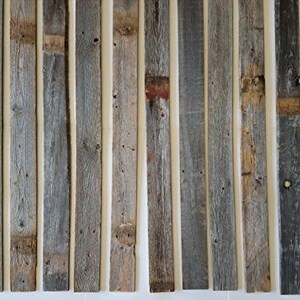 K&ouml;nnte beinhalten: Eine Sammlung von wiederverwendeten Holzbrettern, jedes mit einer einzigartigen verwitterten grauen und braunen Farbe. Die Bretter sind vertikal angeordnet und haben einen rustikalen, abgenutzten Look.