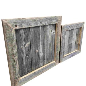 May include: Two rustic wooden picture frames with a distressed gray and white paint finish. The larger frame is slightly angled and the smaller frame is positioned to the right of the larger frame.
