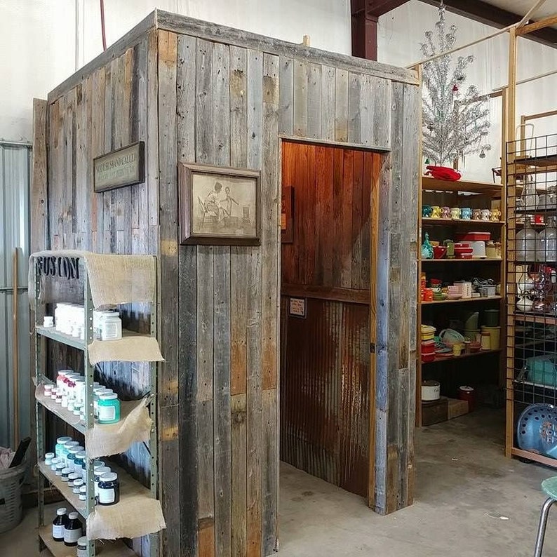 K&ouml;nnte beinhalten: Ein rustikaler Holzraum mit einer T&uuml;r, die zu einem Raum mit einer Metallwand f&uuml;hrt. Der Raum hat ein Regal mit verschiedenen Gl&auml;sern und Flaschen. Die Holzwand hat ein Schild mit der Aufschrift "The Old Trading Post".