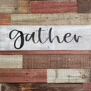 May include: Whitewashed wooden sign with the word "gather" written in black cursive script.