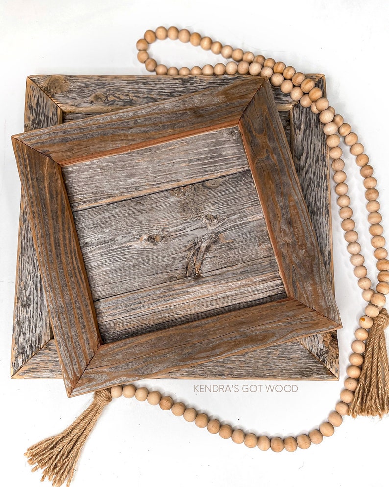 May include: Two wooden picture frames with a rustic, weathered finish, stacked on top of each other. A strand of wooden beads with tassels hangs over the frames. The text "Kendra's Got Wood" is visible on the bottom frame.