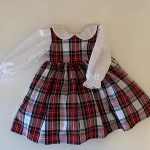 May include: A red and white plaid dress with a white Peter Pan collar and long white sleeves. The dress has a full skirt and is perfect for a special occasion.