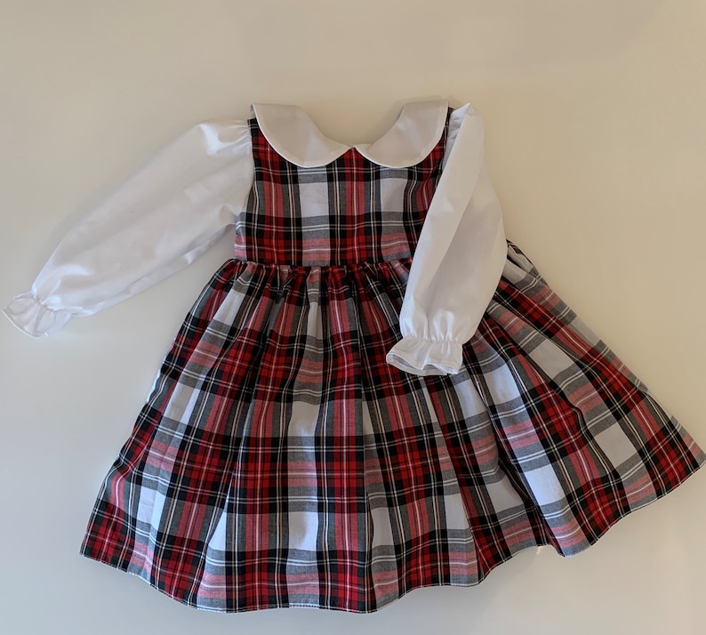 May include: A red and white plaid dress with a white Peter Pan collar and long white sleeves. The dress has a full skirt and is perfect for a special occasion.