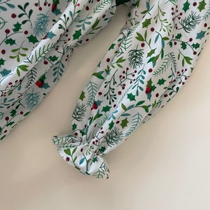 Op de afbeelding: Witte stof met een groen en rood bloemenpatroon. De stof heeft een gerimpelde rand en een groen lint.