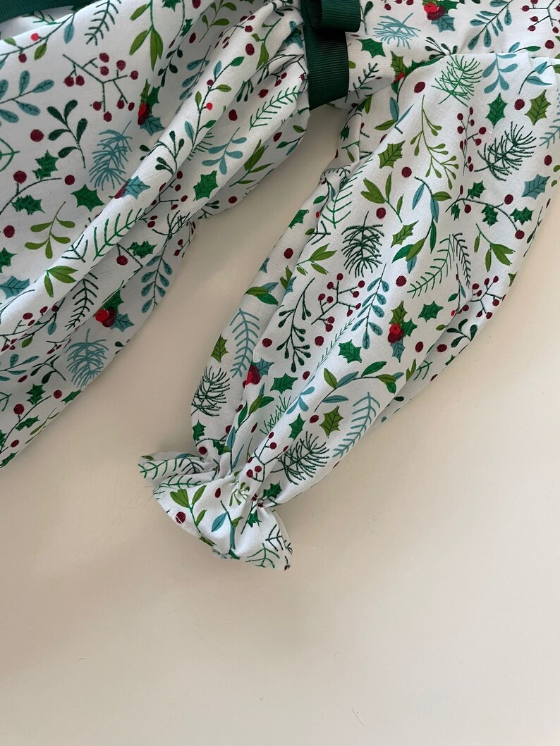 Op de afbeelding: Witte stof met een groen en rood bloemenpatroon. De stof heeft een gerimpelde rand en een groen lint.