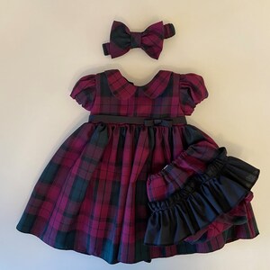 May include: A plaid dress with a black bow and matching headband. The dress has a black belt and a ruffled black underskirt.