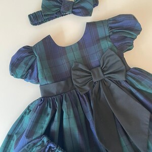 Peut inclure: Une robe &agrave; carreaux verts et bleus avec un n&oelig;ud noir et un bandeau assorti. La robe a des manches bouffantes et une jupe ample.