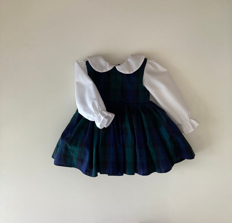 May include: A plaid dress with a white Peter Pan collar and long sleeves. The dress has a blue and green plaid pattern and a full skirt.