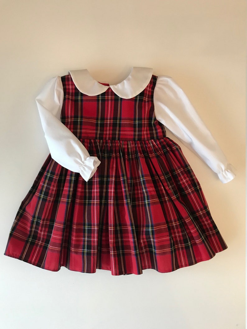 May include: A red and black plaid dress with a white Peter Pan collar and long sleeves. The dress has a gathered skirt and is made of a soft, comfortable fabric.