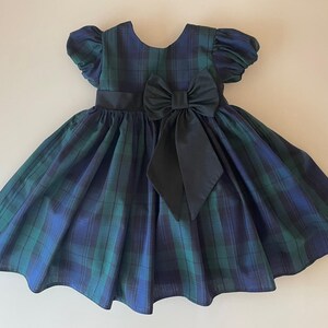 Peut inclure: Une robe &agrave; carreaux bleus et verts avec un n&oelig;ud noir &agrave; la taille. La robe a des manches bouffantes courtes et une jupe ample.
