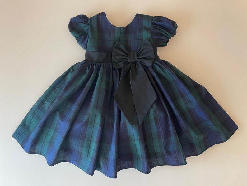 Peut inclure: Une robe &agrave; carreaux bleus et verts avec un n&oelig;ud noir &agrave; la taille. La robe a des manches bouffantes courtes et une jupe ample.